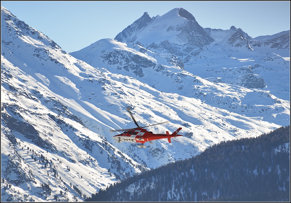 Agusta A109SP Da Vinci der Rega mit der Registrierung HB-ZRR dreht über dem Flughafen Samedan ab, vor der Kulisse des Piz Bernina, dem höchsten Berg und einzigen Viertausender der Ostalpen. Januar 2020.