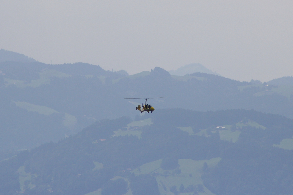 Ein Tragschrauber fliegt in den Bergen beim Bodensee vorbei; fotografiert von dem 1.064m hohen Berg Pfnder (07.08.10)