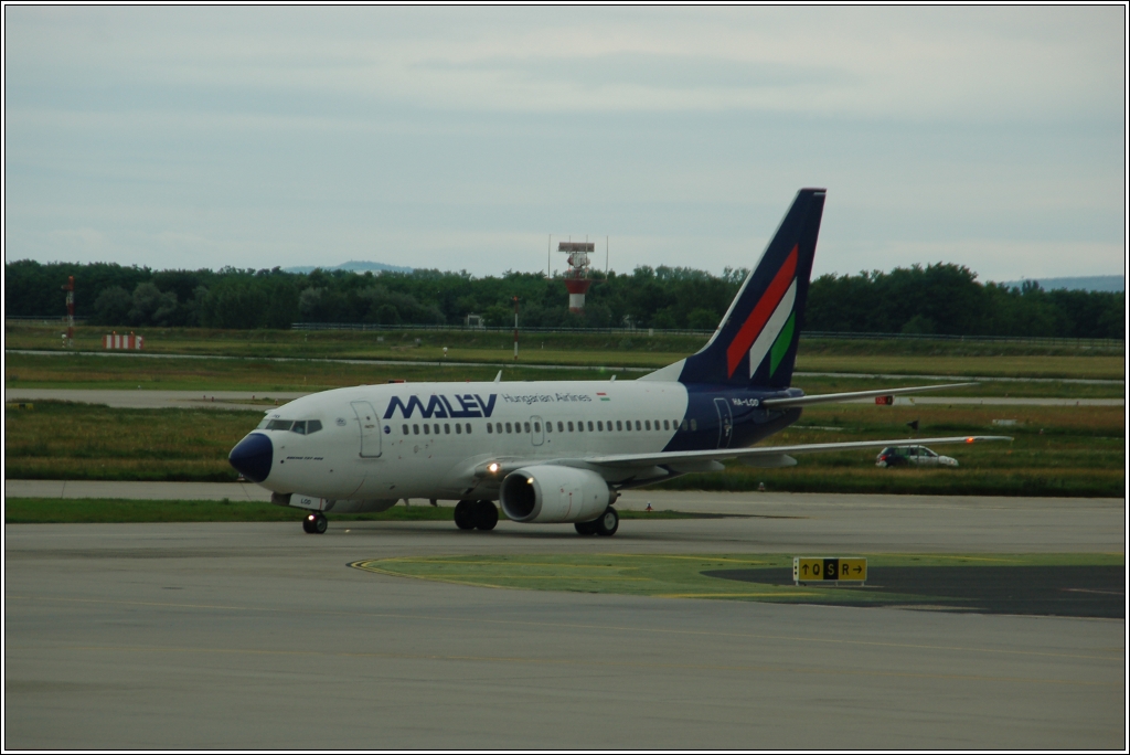 Malv HA-LOD (Boeing 737-600) ist gelandet und fhrt jetzt zu einem Rssel  des Flughafens Budapest-Ferihegy (BUD) um die Fluggste 'frei zu lassen', 21. Juni 2010 (fotografiert aus der Abfahrtshalle).