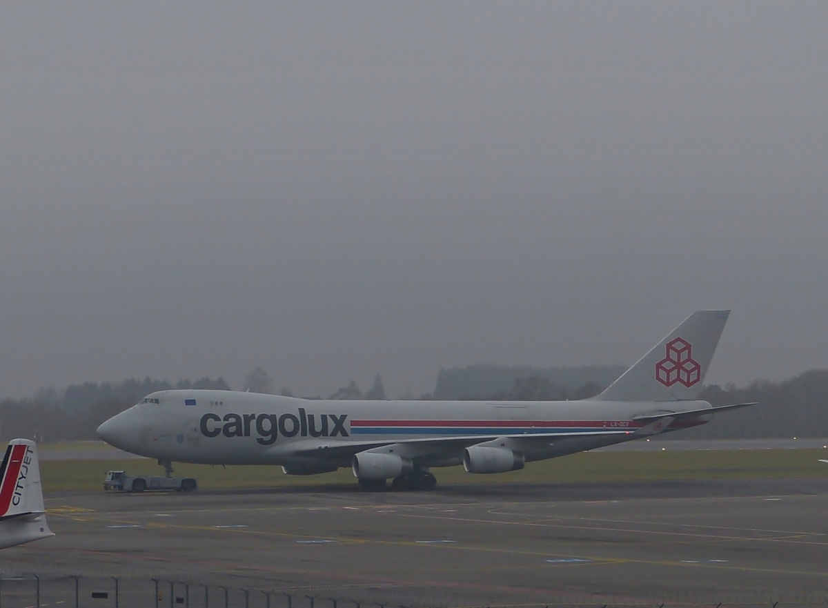 Die Cargolux Boeing 747-4B5 LX-DCV wird am 22.01.2014, bei neblig trbem Wetter, ber das Vorfeld des Flughafens von Luxemburg geschleppt. 