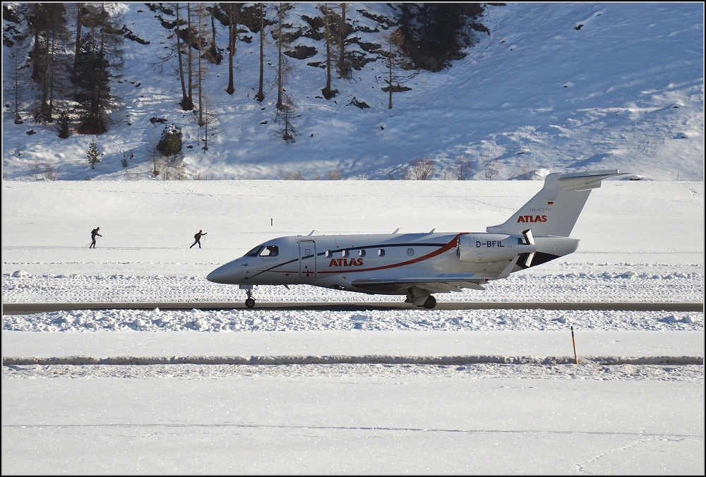 Embraer EMB-545 der Atlas-Air D-BFIL bremst auf der Landebahn, während die Langläufer dahinter Gas geben. Samedan, Januar 2020.