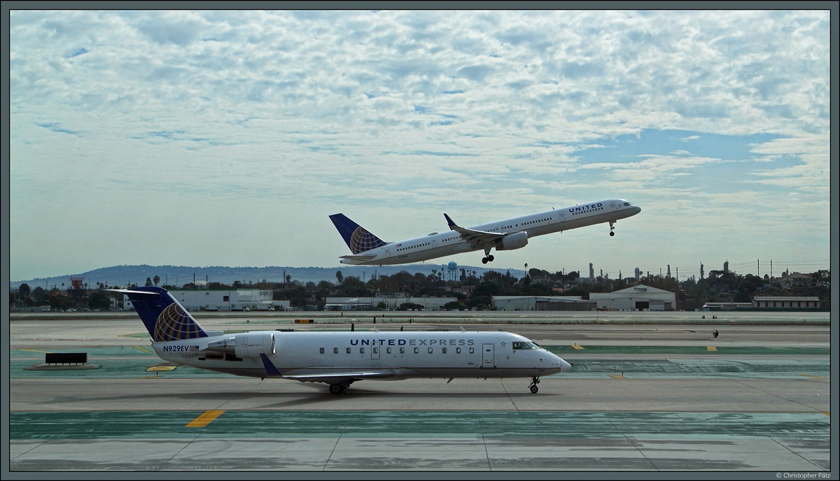 United in groß und klein: Während vorn die Bombardier CRJ-200ER N929EV der Regionalfluggesellschaft United Express (durchgeführt von SkyWest Airlines) über das Vorfeld rollt, hebt im Hintergrund die Boeing 757-33N N77865 der Muttergesellschaft United Airlines ab. (Los Angeles, 29.10.2016)