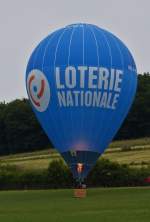 . LX-BLN, Heißluftballon mit der Werbung für die Loterie Nationale, ist an einem Hang nahe Wiltz gelandet, nachdem die Helfer in Anmarsch sind versucht der Ballonfahrer nochmal mit Hilfe des Gasbrenners, dem Ballon abzuheben damit der Korb von den Helfern auf dem nahen Weg gezogen werden kann.  20.06.2015