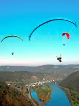 In der Abenddämmerung schweben drei Gleitschirmflieger hoch über der Mosel in Richtung  Hatzenport mit seinen Weinbergen und dem Werth (9. März 2014).